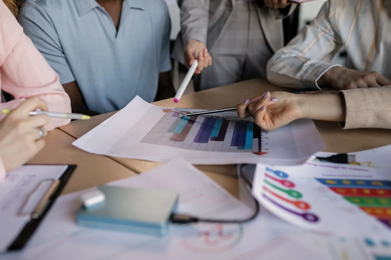 Equipe reunida em uma mesa analisa gráficos e um painel de marketing digital em papel durante uma reunião de planejamento para empresas locais em Curitiba, com anotações e dados.